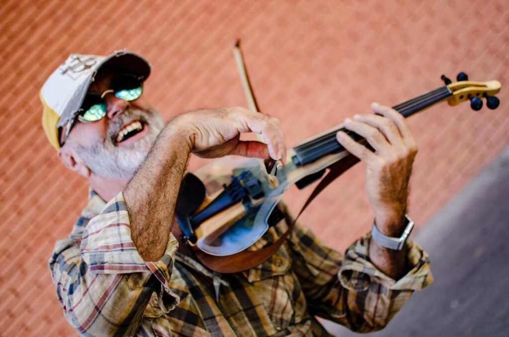 Edison Mouriño tocando un violín eléctrico al aire libre, con gorra y lentes de sol